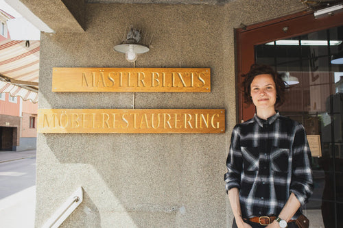 Pernilla Blixt framför skylten till Mäster Blixt Möbelrestaurering