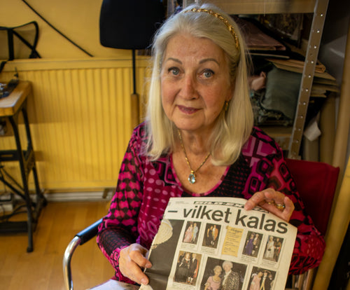 Inger Löwe håller upp en tidningsartikel i sin skrädderiateljé