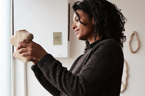 Sophie Sellu håller upp en skulptur i spaltat trä i sin ateljé